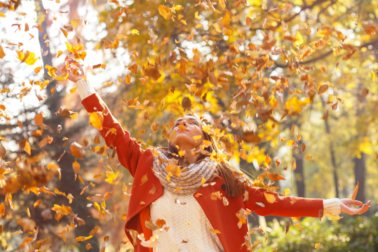 Une femme ouvre ses bras dans un nuage de feuilles d'automne